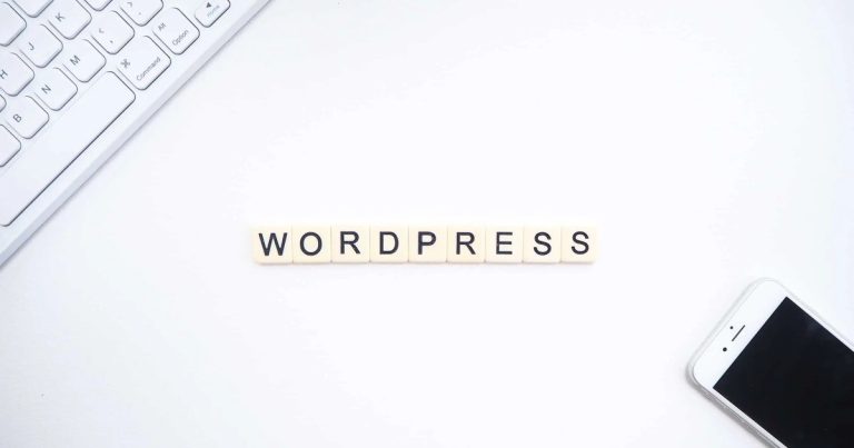 Le mot "WORDPRESS" écrit en lettres, accompagné d'un clavier et d'un smartphone, disposés sur un bureau blanc.