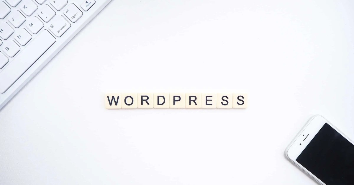 Le mot "WORDPRESS" écrit en lettres, accompagné d'un clavier et d'un smartphone, disposés sur un bureau blanc.