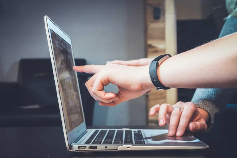 Personne pointant un écran d'ordinateur portable et une autre main d'une autre personne sur le clavier