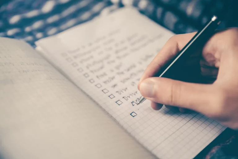 Main écrivant check-liste des tâches sur un carnet