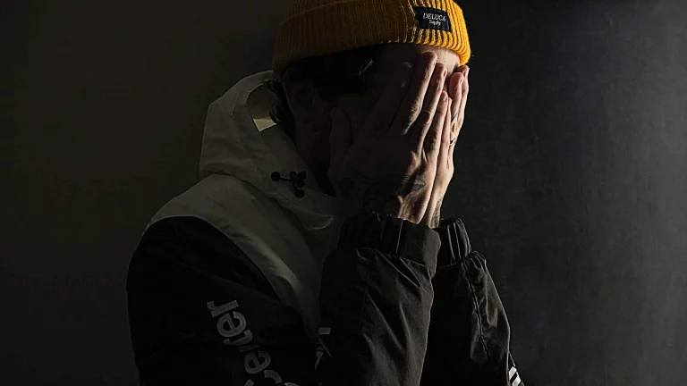 Homme cachant visage, bonnet jaune, fond sombre