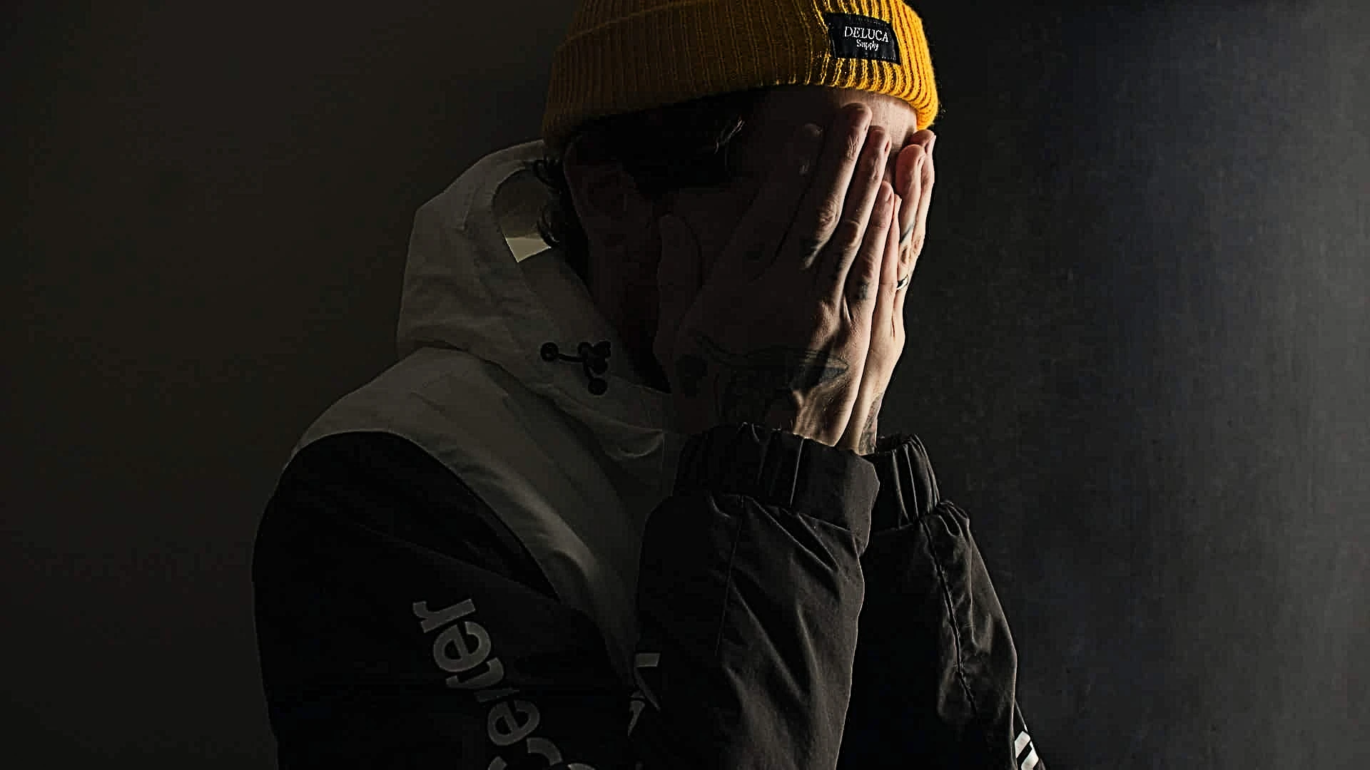 Homme cachant visage, bonnet jaune, fond sombre
