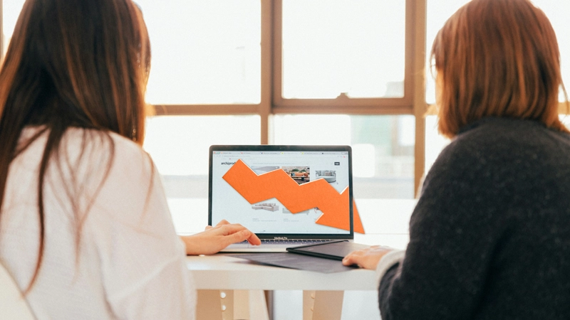 Two people review website data on a laptop, while a downward arrow illustrates a decline.