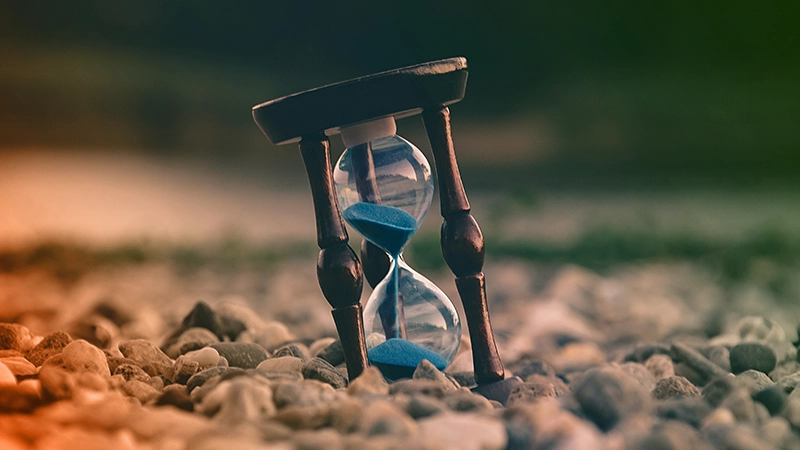 Un sablier au sable bleu, délicatement posé sur des pierres grises et blanches, évoque une harmonie subtile entre le temps et la nature.