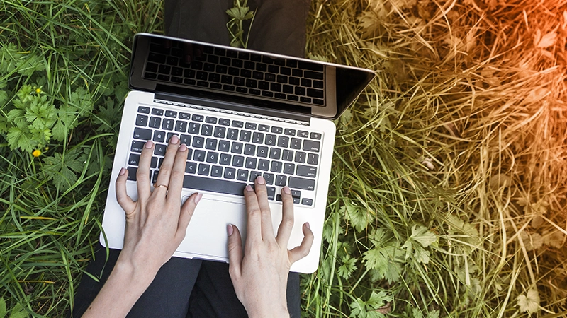 Une femme assise dans un jardin travaille sur son ordinateur portable.